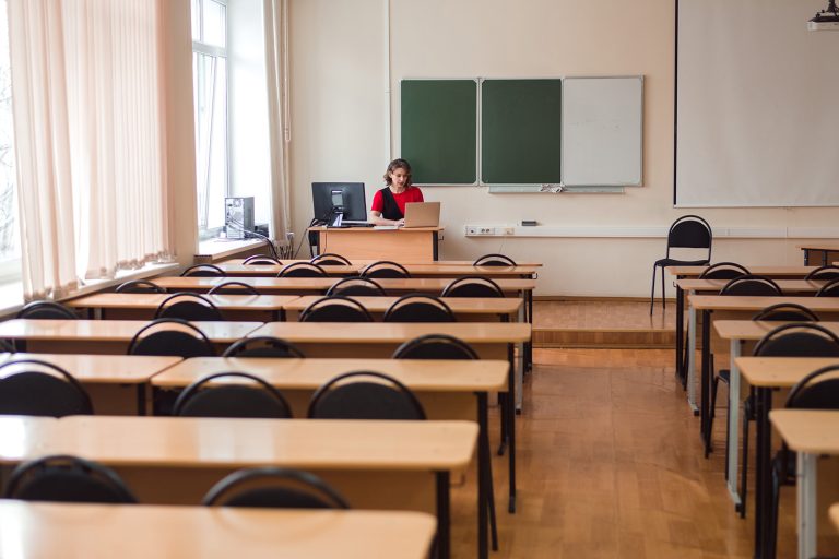 teacher-in-empty-classroom-using-laptop-2022-11-14-20-11-51-utc